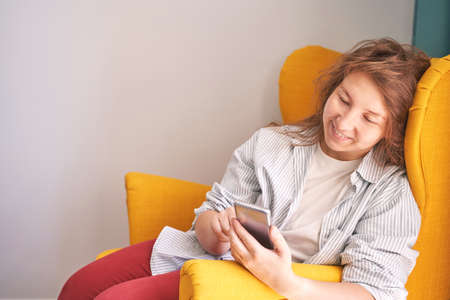 Pretty young woman texting by phone. Happy female person indoors. Business portrait. Lady sms friends. Cute adult students at home. Online educationの写真素材