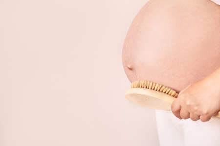 Pregnant skin care. Body brush routine. Woman belly peeling. Female person drainage scrub. Wooden massage. Anti cellulite cosmetology treatmentの写真素材