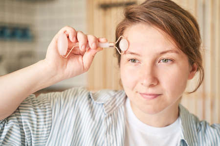 Young woman doing morning routine. Home maternity treatment. Health care concept. Female person. Pandemic concept. Guasha acupunture face massageの写真素材