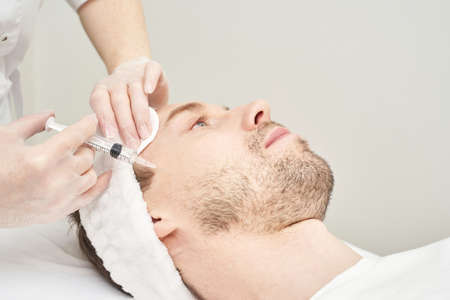 Injection at spa salon. Doctor hands in gloves. Closeup. Pretty male patient. Beauty treatment. Healthy skin procedure. Young man face. Plasmolifting rejuvenationの写真素材