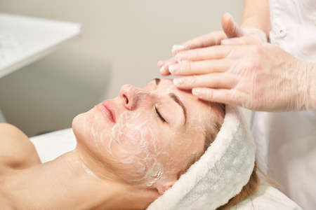 Face massage prepare at spa salon. Doctor hands. Pretty female patient. Beauty treatment. Healthy skin procedure. Young woman head. Cleaning rejuvenation. Facial dermatology mask. Detox therapyの写真素材