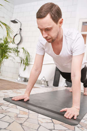 Mature man doing yoga exercise at home. Health care online lessons. Indoor fitness workout. Remote...