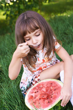 Funny female kid with watermelon slice. Summer child picnic. Kindergarden snack. Sweet natureal food. Red berry. Holding juicy vegetarian productの写真素材
