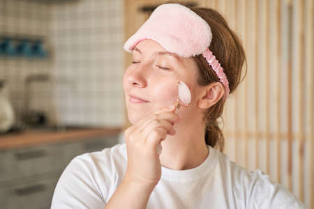 Young woman doing morning routine. Home maternity treatment. Health care concept. Female person. Pandemic concept. Guasha acupunture face massageの写真素材