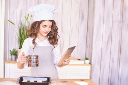 Young girl cooking at kitchen. Curly pretty child portrait. Chef student. Attractive brunette. Children emotion. People baking in cook hat and apronの写真素材