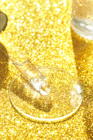 Serum gel texture swatch. Transparent drop with golden sparkles. Yellow bokeh background. Face skincare product. Liquid oil essence. Beauty collagen splash. Organic peeling treatment. Body health careの写真素材