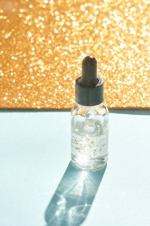 Luxurious gold-infused skin serum bottle on soft blue surface with glittering backgroundの写真素材