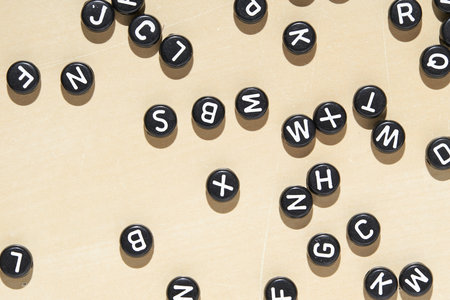 Scattered black alphabet letter beads on beige background for creative education and craft designsの写真素材