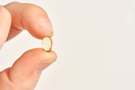 Hand holding small yellow pill on white background for health and medicine conceptの写真素材