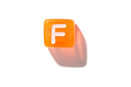 Orange cube with white letter f casting shadow on white background.の写真素材