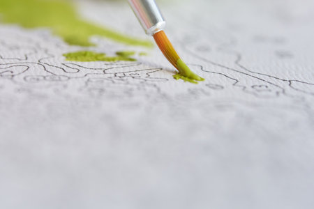 Close-up of a paintbrush adding green to a detailed paint-by-numbers canvas.の写真素材