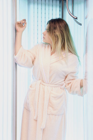 Woman in bathrobe relaxing inside sunbed tanning booth - indoor spa and wellness concept for self-care and leisure.の写真素材