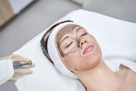 Woman undergoing laser facial treatment with protective headband in modern skincare clinic.の写真素材