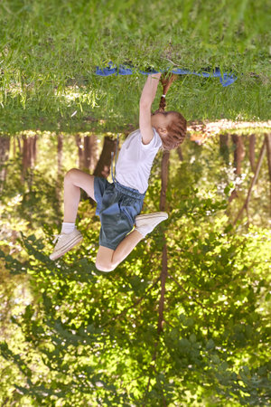 Playful child enjoying outdoor zip line adventure in lush green park setting with sunlit background.