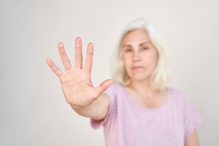 Senior woman gesturing stop with open hand, emphasizing communication and social awareness.の写真素材