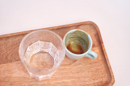 Minimalist coffee setup with espresso cup and water glass on wooden tray in soft natural light.