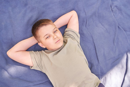 Contemplative boy relaxing on blue blanket outdoors on a sunny day.
