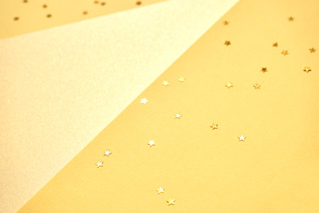 Glittering gold stars on textured yellow paper background for festive celebrations and creative...