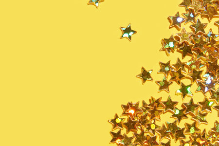 Festive golden glitter stars on vibrant yellow background for celebrations and party themes.の写真素材