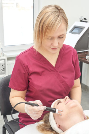 Female caucasian adult aesthetician performing facial treatment on female client with modern...