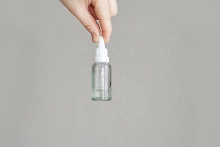 Hand holding clear dropper bottle on gray background for skincare or essential oils display.