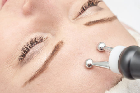 Caucasian female receiving facial microcurrent therapy at spa for skin rejuvenation and anti aging benefits.の写真素材