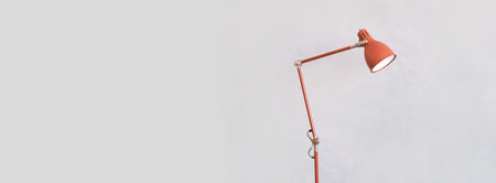 Minimalist orange desk lamp with adjustable arm against light background.の写真素材