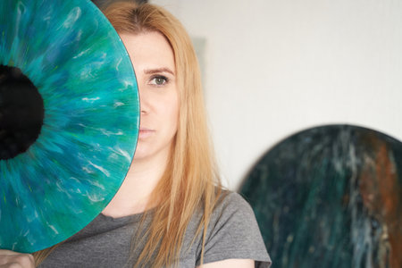 Young caucasian female with long blonde hair holding abstract blue circular art piece in gray shirt...