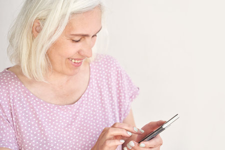 Elderly caucasian female smiling while using smartphone in casual polka dot shirt.