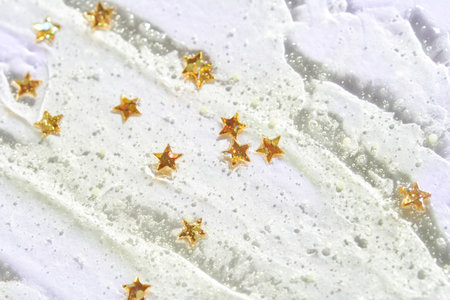 Golden star confetti on shimmery white texture with glitter and bubbles creating festive atmosphere.