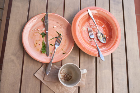 Empty orange plates and dirty coffee cup on wooden table after meal with used utensils.