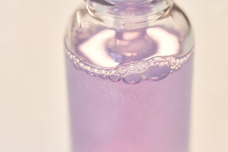 Close-up of a lavender-tinted liquid in a small glass bottle with bubbles floating on the surface.の写真素材