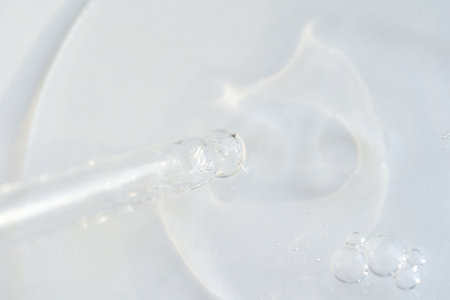 Close-up of transparent glass dropper with water droplets on white background.の写真素材