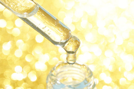 Golden liquid droplet falling from pipette into bottle on sparkling background.の写真素材