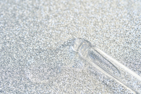 Transparent glass dropper on sparkling silver glitter background texture shine.の写真素材