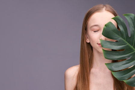 Young caucasian female with long hair and monstera leaf on gray background portrait.の写真素材