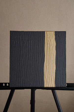 Textured black canvas painting with golden vertical line on easel in minimalist setting.の写真素材