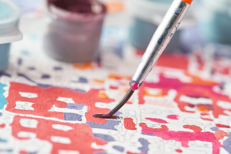 Close up of paintbrush on colorful paint by numbers canvas with blurred paint pots in background.の写真素材