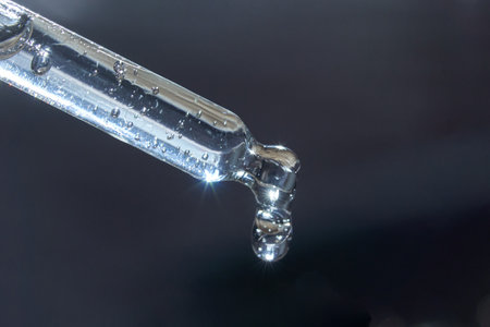 Close-up of transparent glass dropper with droplet against dark background.の写真素材