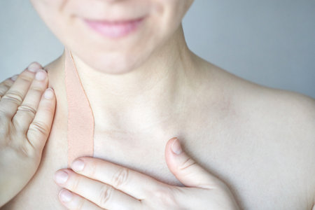 Female adult caucasian applying therapeutic kinesiology tape to shoulder neck area for pain relief.の写真素材
