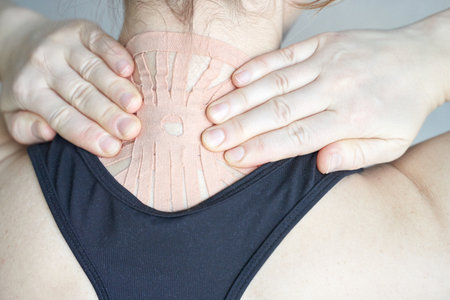 Young caucasian female applying therapeutic tape on neck for pain relief and muscle support.の写真素材