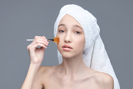 Young caucasian female applying makeup after shower with towel wrapped on head.の写真素材