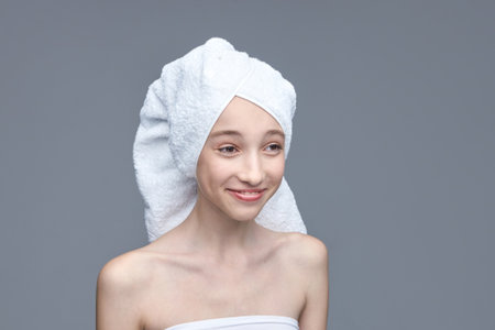 Young caucasian female with towel wrapped hair smiling on gray background.の写真素材