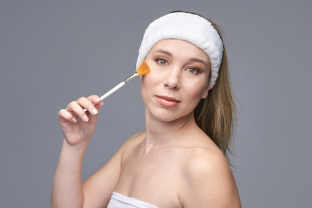 Caucasian female adult applying makeup with brush on cheek in skincare routine.の写真素材