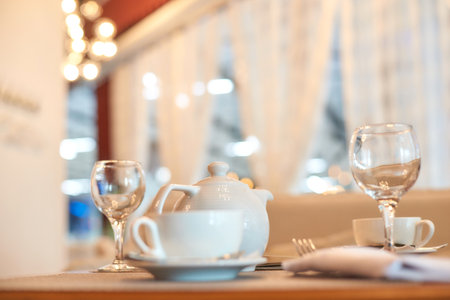 Elegant table setting with white teapot and glassware in cozy cafe ambiance.の写真素材