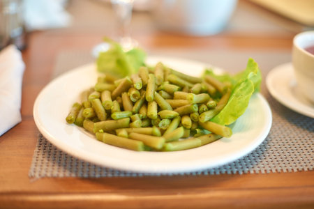 Delicious cooked green beans on white plate with lettuce garnish in warm dining setting.の写真素材