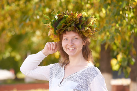 Smiling caucasian female adult wearing autumn leaf crown in sunlit park.の写真素材