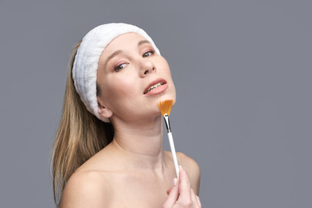 Caucasian adult female applying makeup with brush wearing white headband.の写真素材