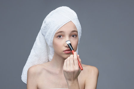 Young caucasian female applying makeup with brush on her face in skincare routine.の写真素材