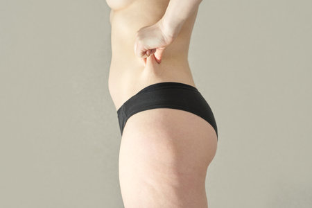 Caucasian mature female showing skin elasticity and stomach pinch in black underwear side view.の写真素材